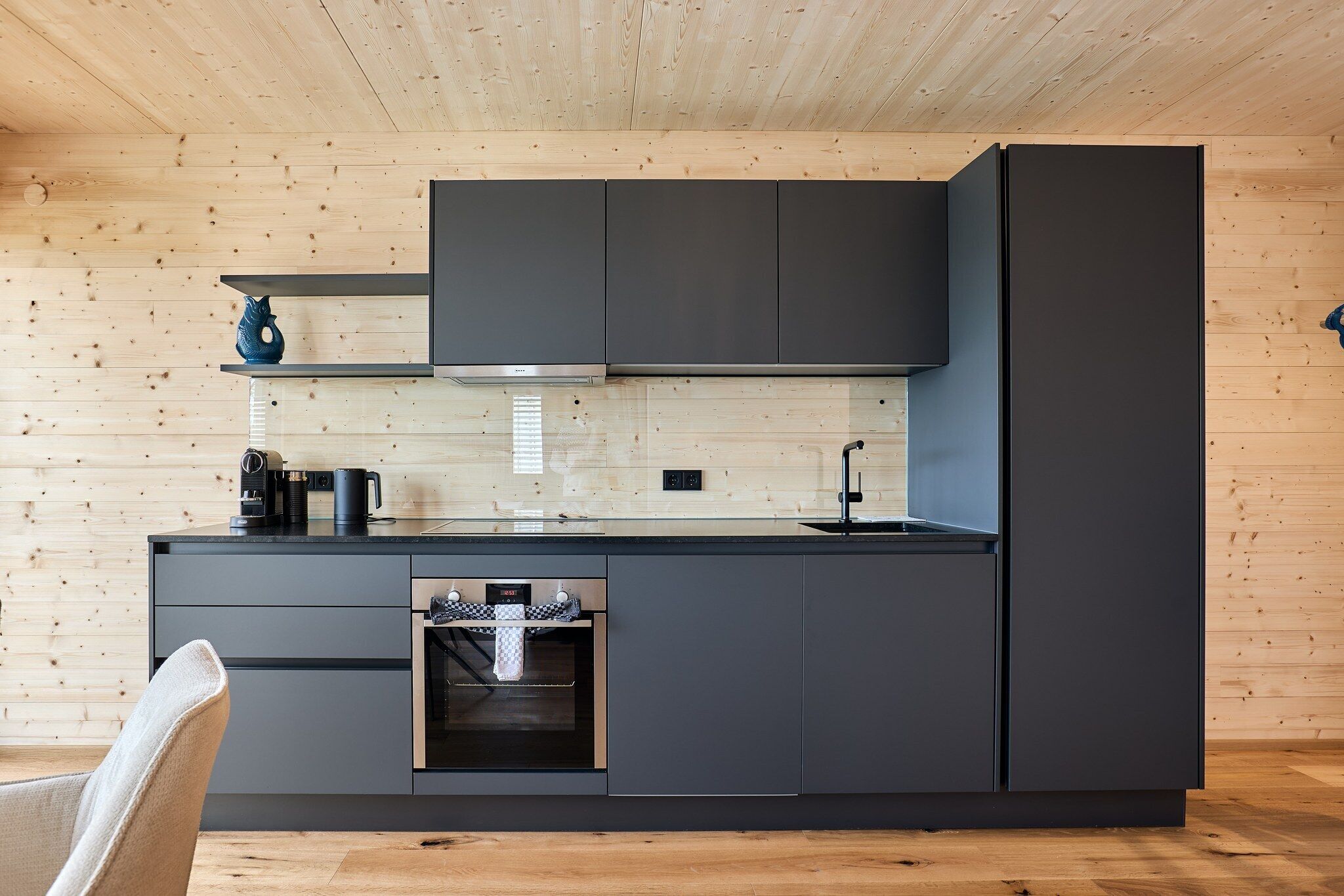 A modern kitchen with dark cabinetry, a built-in oven, and a wooden ceiling.