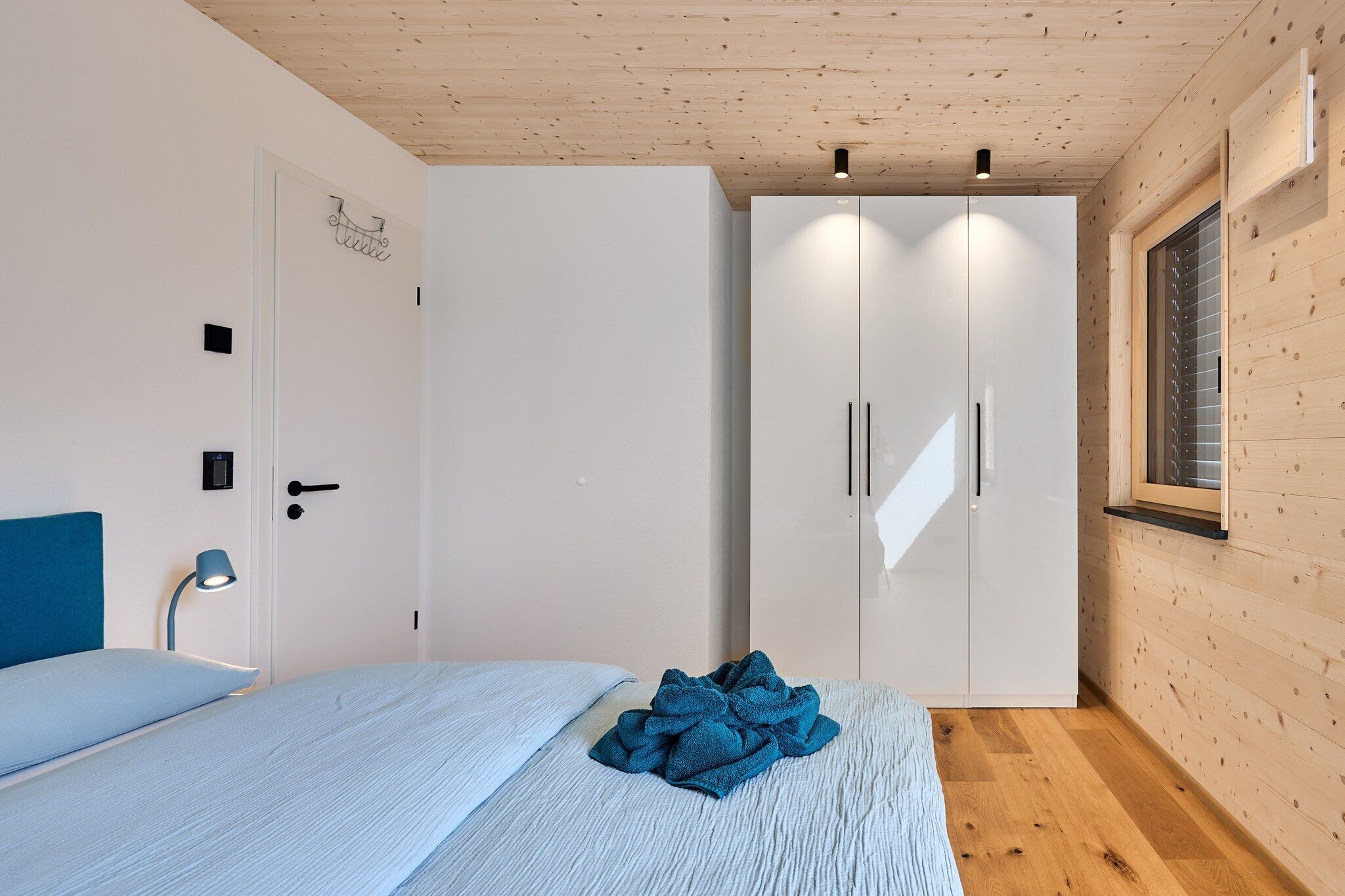 Een slaapkamer met een bed, een kledingkast, een bedlampje en een raam met jaloezieën.