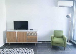 A room with a TV on a white cabinet, a green armchair, and an air conditioning unit on the wall. - Studio 2 pers air-conditioned 600m from the beach with private parking and terrace (La Grande-Motte)