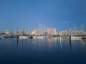 A marina with multiple boats docked, a clear sky, and buildings in the background. - Studio for 2 people, air-conditioned, 600 meters from the beach, with private parking and a terrace (La Grande-Motte)