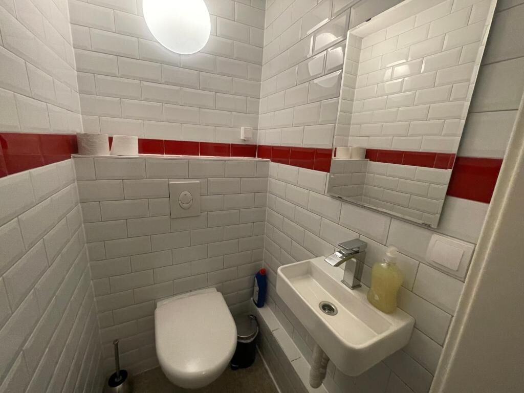 A small bathroom with white tiles, a red accent wall, a white toilet, a sink, and a mirror.