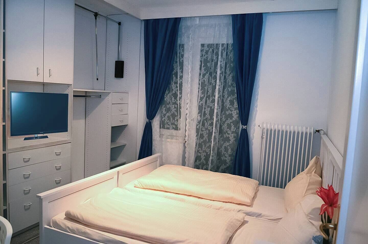 A bedroom with a bed, a TV, a wardrobe, and a radiator.