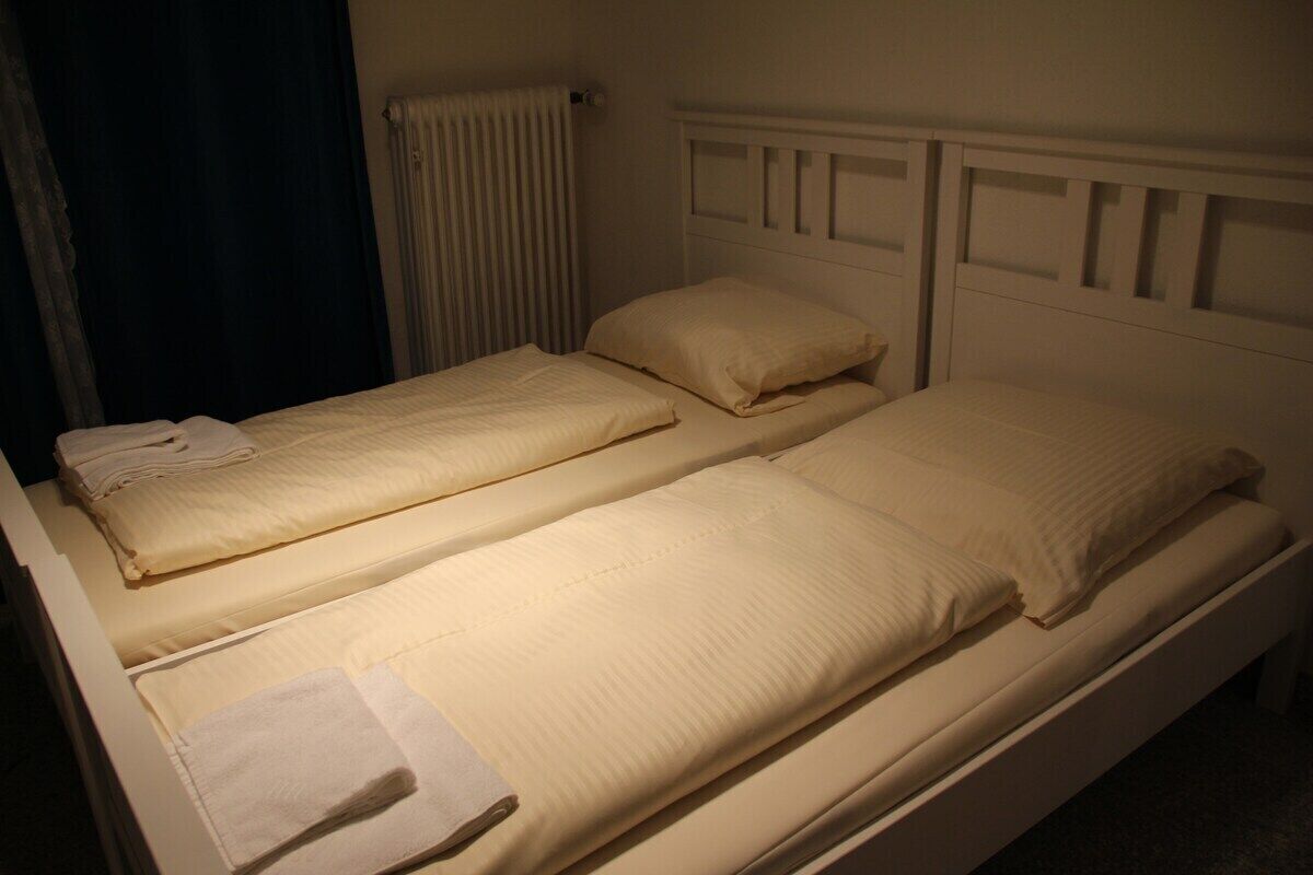 Un lit jumeau avec une tête de lit blanche et un lit simple au design similaire.