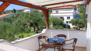 Un'area salotto esterna riparata, con tavolo e sedie, affacciata su un quartiere residenziale con case e vegetazione.