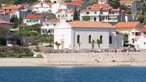 Un borgo costiero con edifici bianchi, tetti rossi e un muro in pietra lungo la spiaggia.