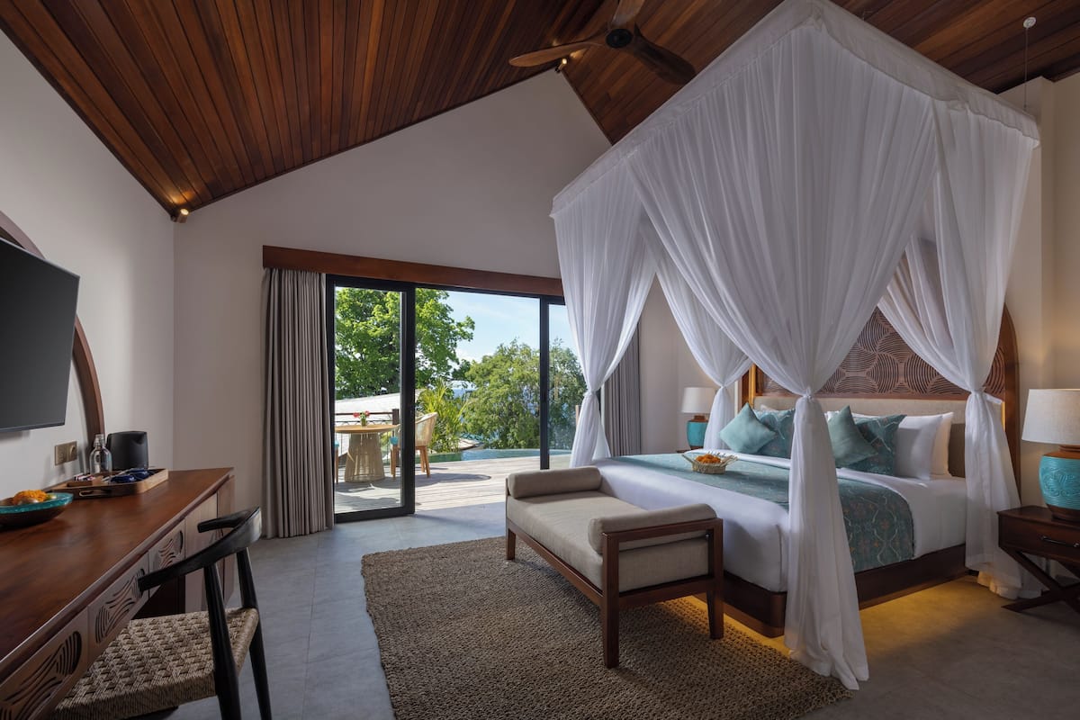 A bedroom with a canopy bed, a desk with a chair, and a view of the outdoors.