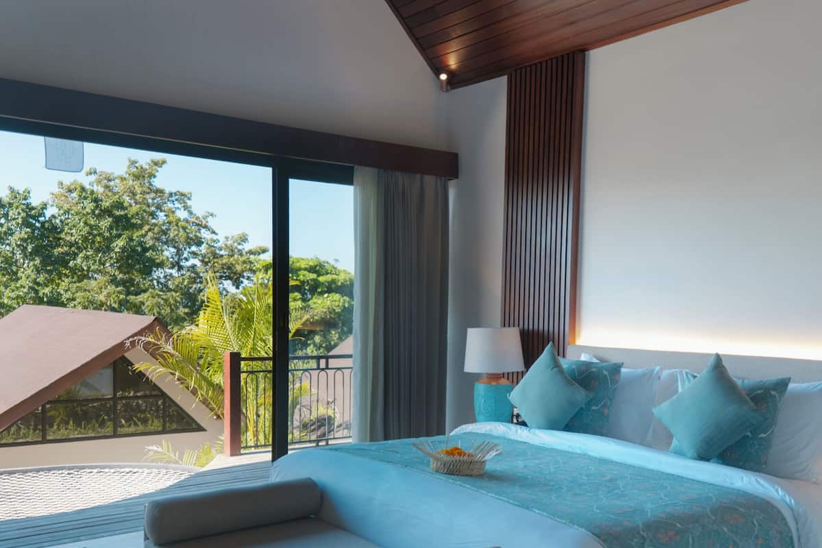 A modern bedroom with a large bed, a bench, a nightstand, and a view of the outdoors.