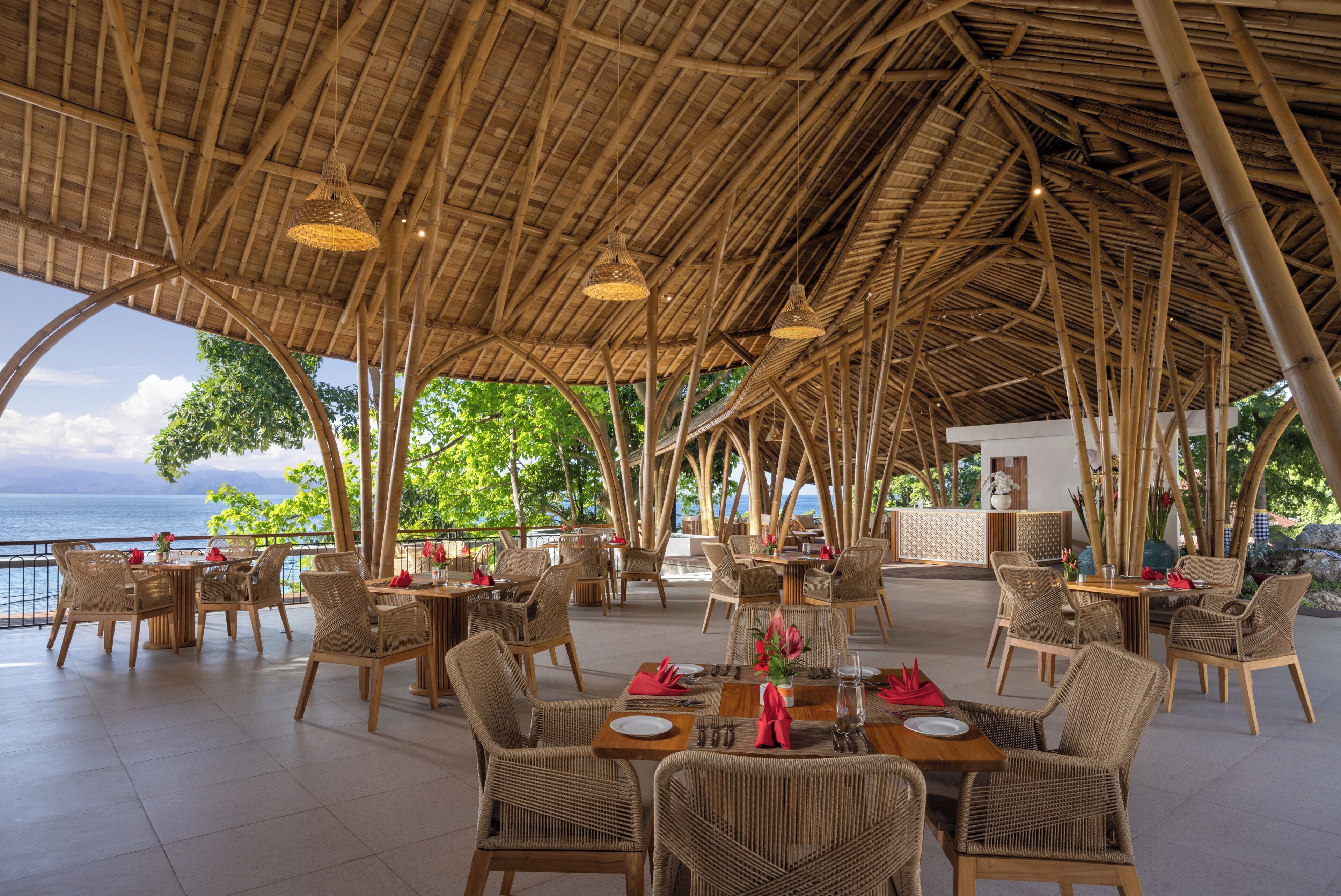 An outdoor dining area with wicker furniture, a thatched roof, and a view of the sea.