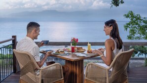Un couple est assis à une table en bois, devant laquelle s’étend une vue sur la mer.