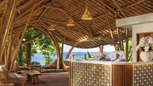 Un espace d’accueil doté d’un plafond en bambou, de meubles en bois et offrant une vue sur la mer.