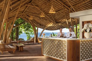 Un área de recepción con techo de bambú, mobiliario de madera y vista al mar.