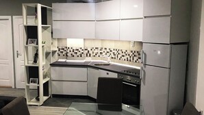 Une cuisine de taille réduite avec des meubles blancs, un plan de travail noir et un pare-feu en carreaux.