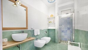 Een badkamer met een grote spiegel, een wastafel, twee douchetjes, een douche met betegelde muren en een witte handdoekhouder.