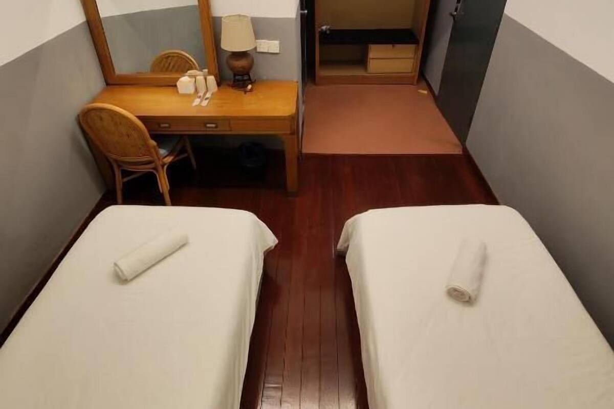 Une petite chambre d’hôtel avec deux lits simples, un bureau avec une chaise, un miroir et une armoire.