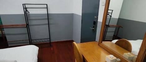 A hotel room with a wooden desk, a bed, a chair, a mirror, and a wardrobe.