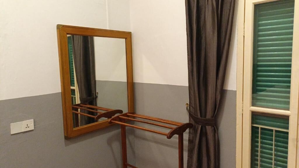 A bathroom with a wooden towel rack, a mirror, a window with green blinds, and a towel hanging on the rack.