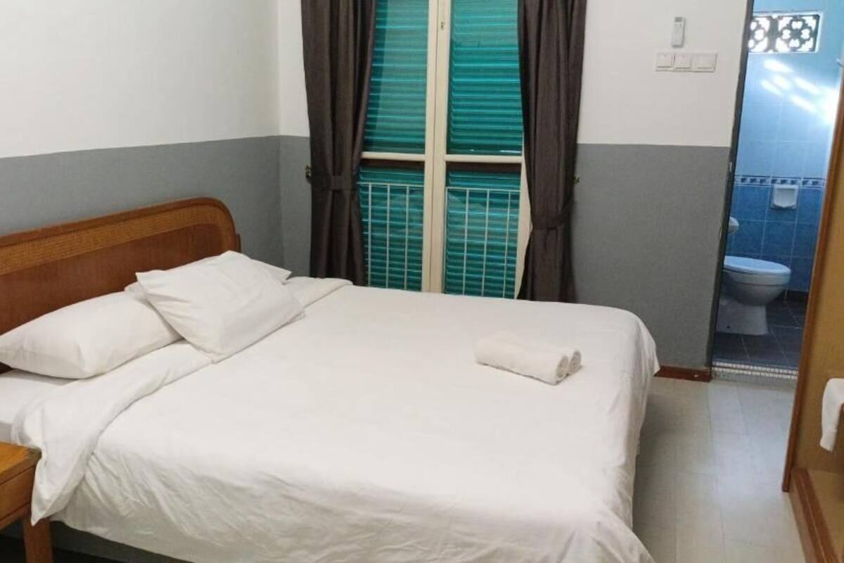 Un lit simple avec une literie blanche, dans une chambre dont la tête de lit est en bois. Une serviette est posée sur le lit.