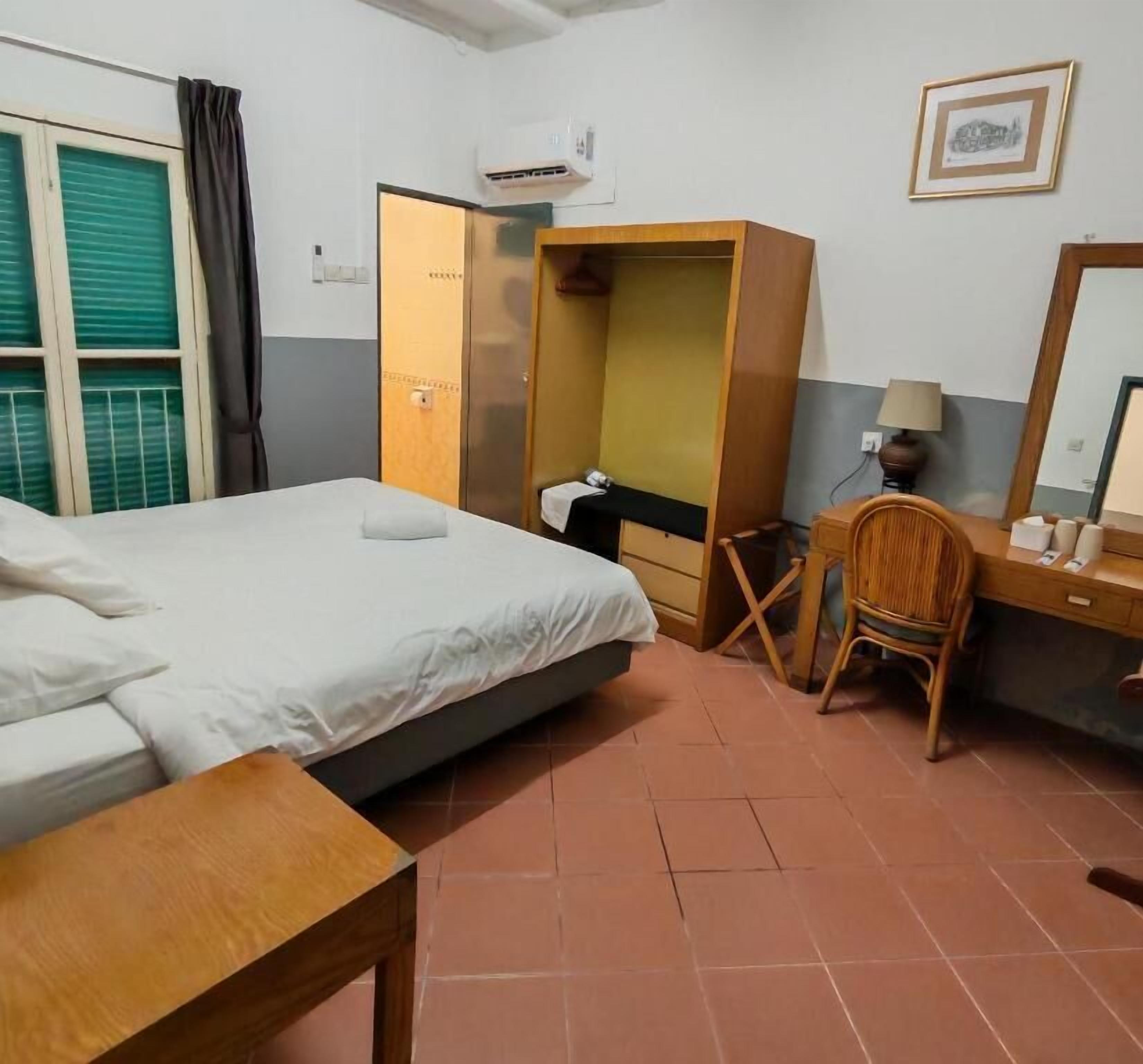 A hotel room with a bed, a desk with a chair, a wardrobe, and a window with curtains.
