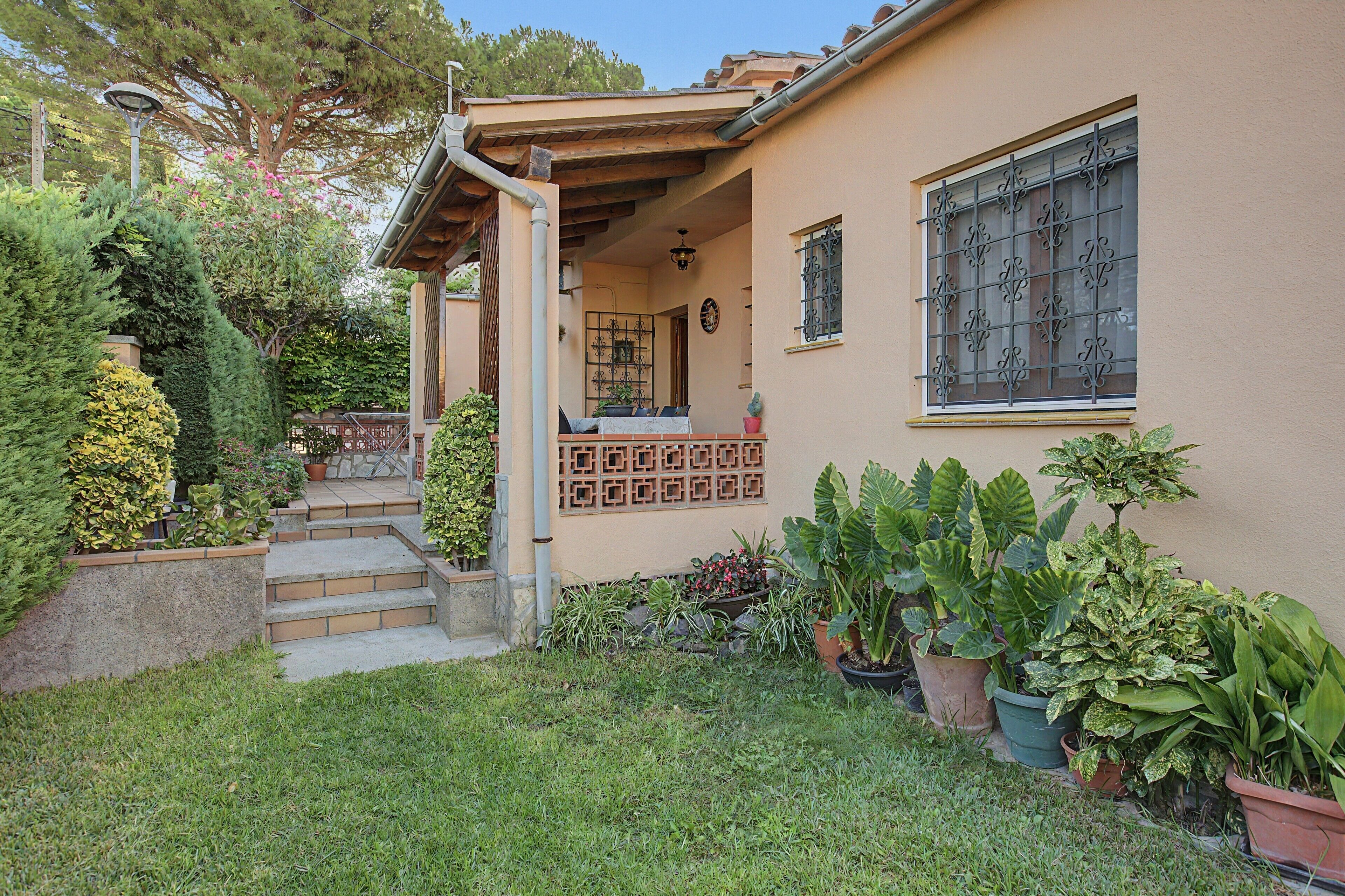 A house with a covered porch, a small garden with various plants, and a window with decorative bars.
