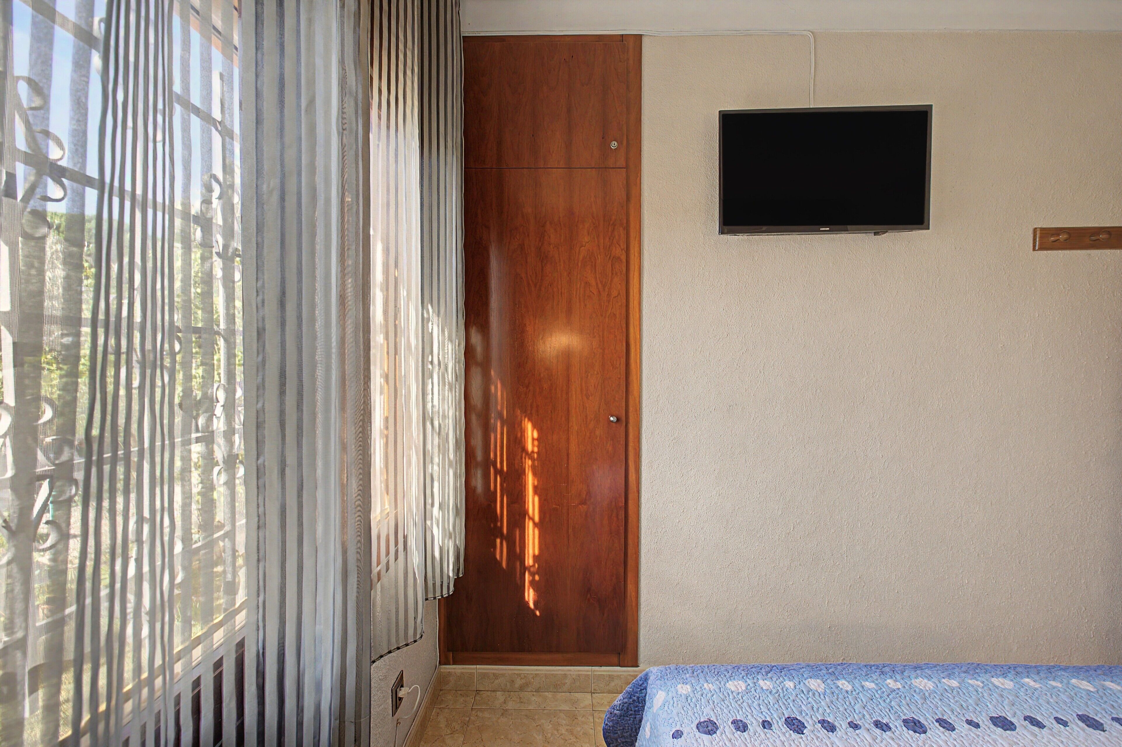 Een kamer met een houten garderobe, een aan de muur bevestigde televisie en een bed met een bedspread met een patroon.