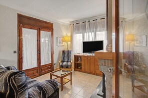 Ein Wohnzimmer mit einer Couch, einem Sessel, einem Fernseher und einem Schrank.