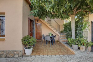 A patio with a table and chairs, a wooden door, and a staircase leading to an upper level. - Holiday Home 'Rocamar' with Mountain View, Private Terrace and Air Conditioning (L'Escala)