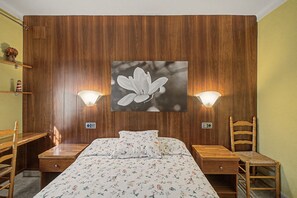 A bedroom with a wooden headboard, a bed with floral bedding, two bedside tables, a chair, and wall-mounted lamps. - Holiday Home 'Rocamar' with Mountain View, Private Terrace and Air Conditioning (L'Escala)