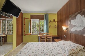 Ein Schlafzimmer mit Bett, Schreibtisch, Stuhl, Fernseher und einem Fenster mit Blick auf Grünflächen.