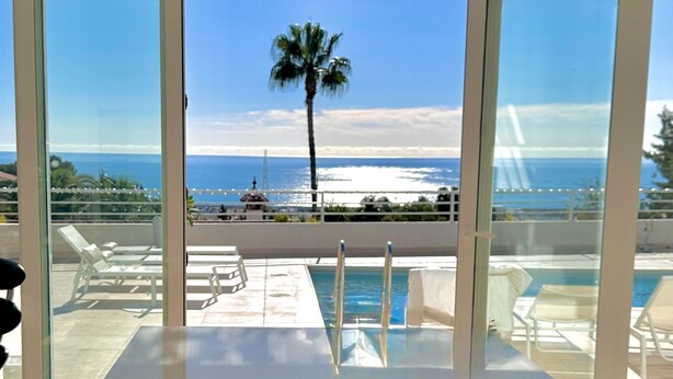 A modern indoor pool area with clear views of the ocean and a palm tree. - Villa Palmeras - Modern luxury with breathtaking sea view (Caleta de Vélez)