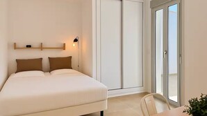 A bedroom with a bed, a bedside table, a chair, a potted plant, and a sliding door to a balcony. - Villa Palmeras - Modern luxury with breathtaking sea view (Caleta de Vélez)