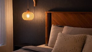 Een slaapkamer met een houten hoofdbord, een hanglamp en een bed met kussens.