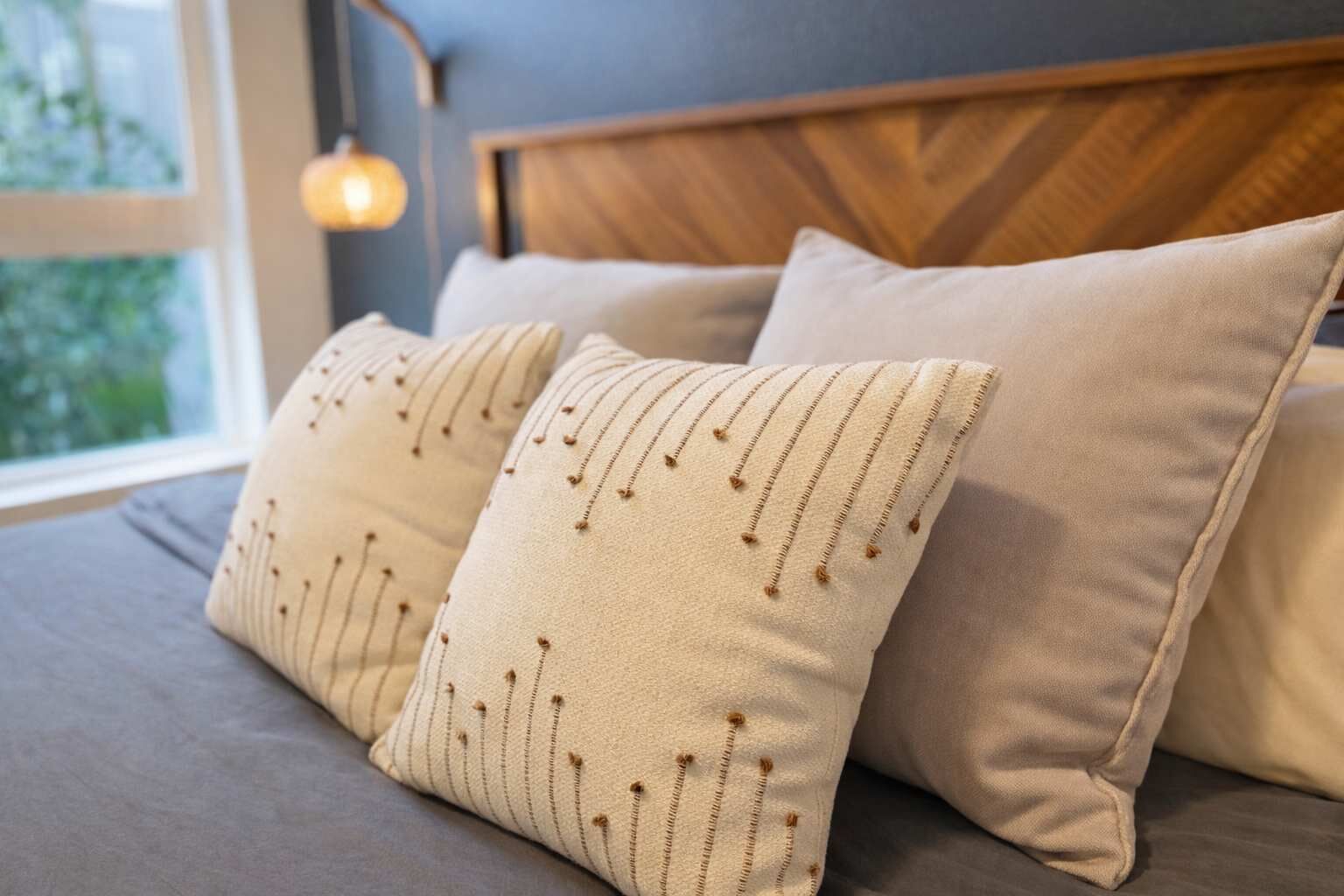 Un lit avec deux oreillers, une tête de lit en bois et une fenêtre laissant entrer la lumière naturelle.