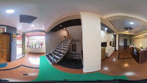 Un atrio d'albergo con una scala, una reception e una zona accoglienza.