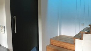 Una stanza moderna con una porta scura, una scala di legno e un muro bianco.