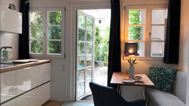 Una cucina compatta con mobili bianchi, un'area pranzo con tavolo e sedie, e vista sul verde.