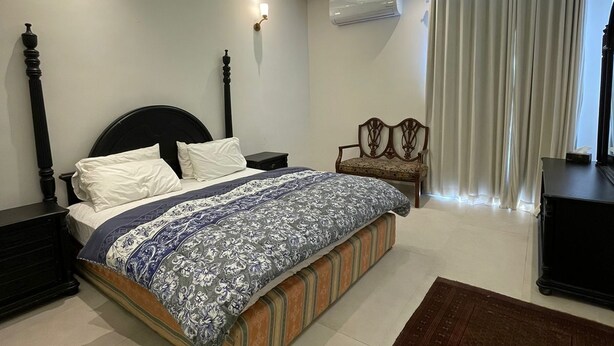 Un dormitorio con cama, mesitas de noche, una silla, un escritorio y una ventana con cortinas.