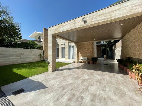 A modern house with a covered patio area, a well-maintained lawn, and potted plants.