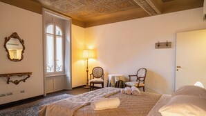 Hotellihuone, jossa on suuri sänky, kaksi tuolia, pöytä, peili ja ikkuna, josta on näkymä.