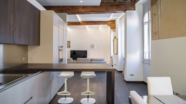 Moderni keittiö, jossa on keskeinen saareke, baarituolit sekä valkoisella pöydällä ja tuoleilla varustettu ruokailutila.