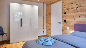 Ein Schlafzimmer mit einem Bett, einem Kleiderschrank, einem Sessel und einem Nachttisch mit Lampe.