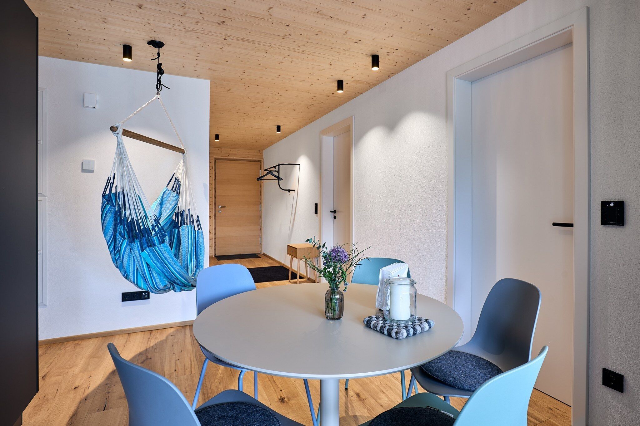 A modern room with a round table, chairs, a hanging chair, and a door.