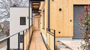 A modern building with a wooden exterior, a narrow corridor, and a small outdoor seating area. - Rosenhof with whirlpool | Grüne Tanne | seeglueck (Konstanz)