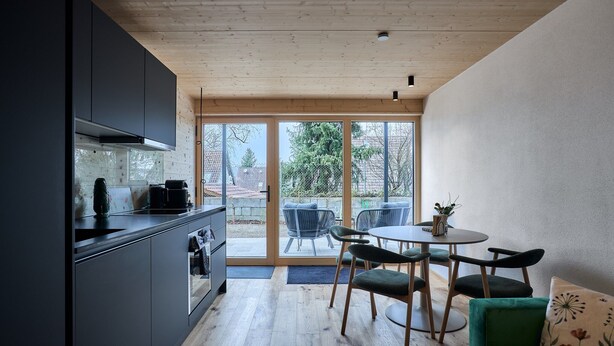 A modern kitchen with dark cabinets, a wooden ceiling, and a dining area with a round table and chairs. - Rosenhof with whirlpool | Grüne Tanne | seeglueck (Konstanz)