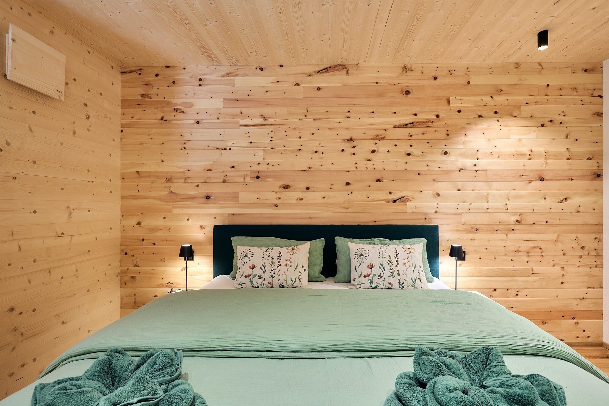 A wooden-paneled room with a bed, two bedside lamps, and a nightstand.