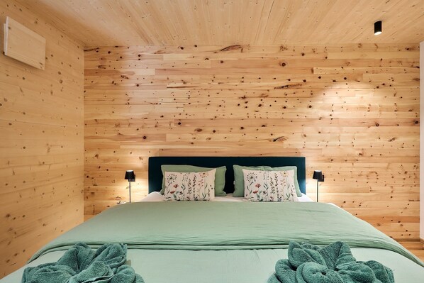 Quarto com painéis de madeira, uma cama, duas luminárias laterais e uma mesa de cabeceira.