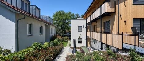 A narrow pathway flanked by buildings with balconies and a small garden area.