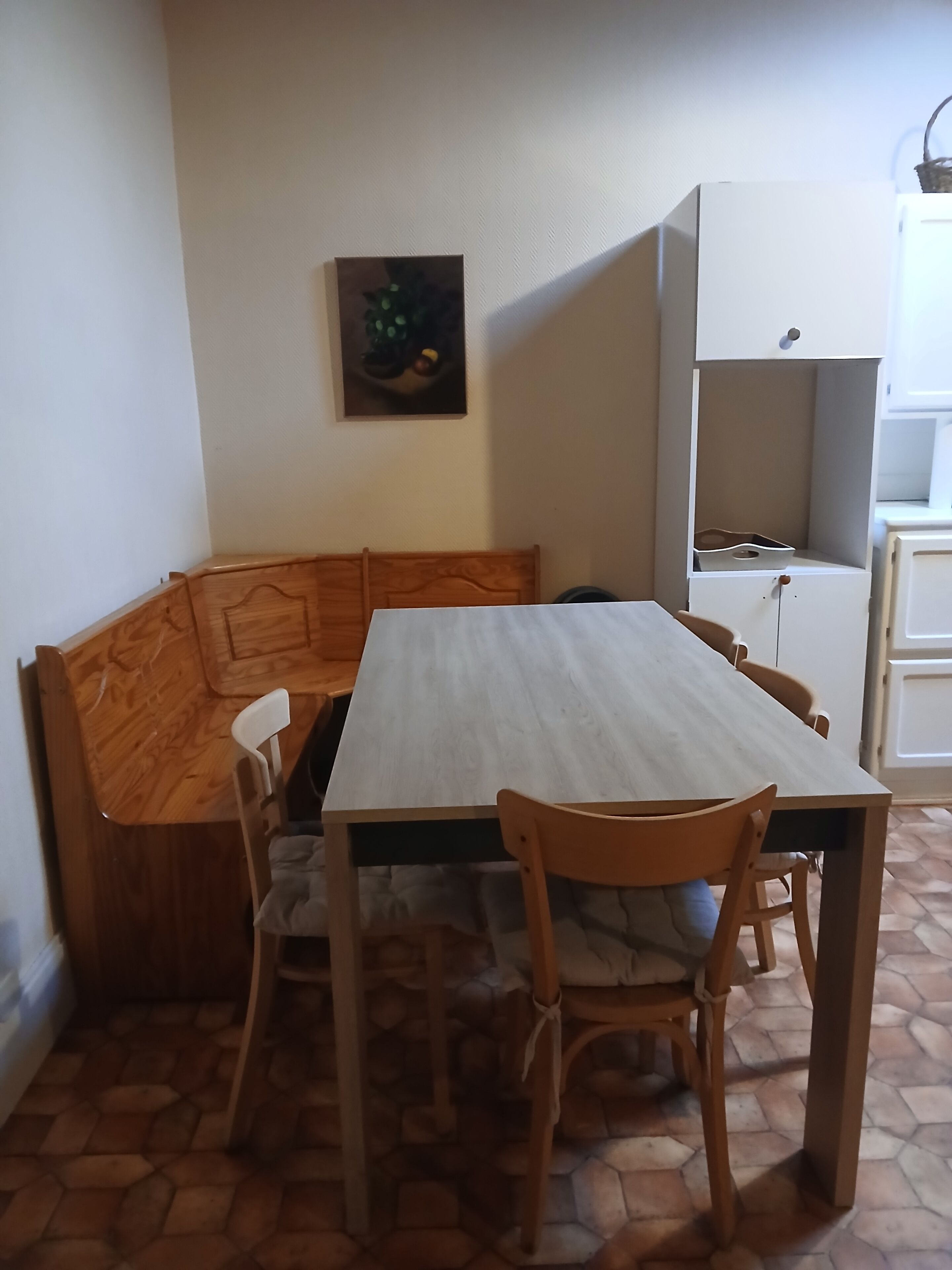 A dining area with a wooden table and chairs, a white cabinet, and a painting on the wall.
