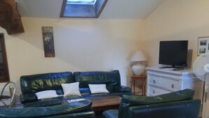 Una sala de estar acogedora con un sofá, dos sillones, una mesa de centro, un televisor y un ventilador de techo.