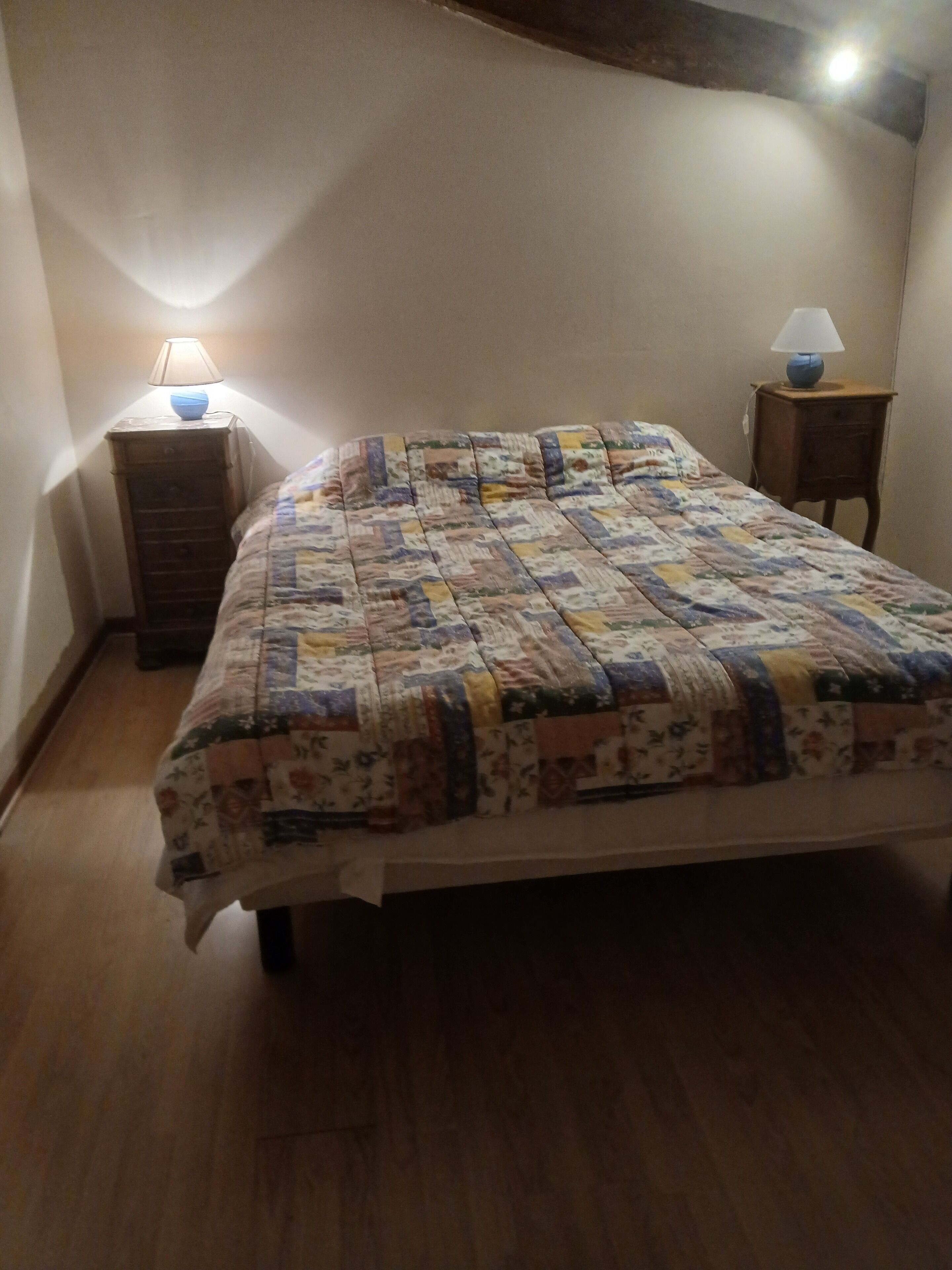 Une chambre à coucher avec une couvre-lit matelassé, deux tables de chevet avec des lampes et un plancher en bois.