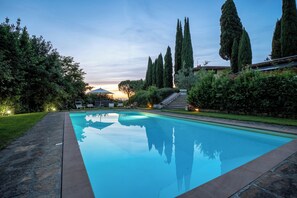 Une piscine bordée de pierres, entourée de verdure et d’arbres imposants.